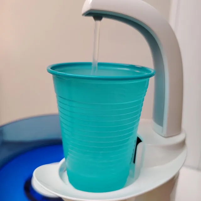 En turkis engangskopp fylles med vann fra en automatisk dispenser på tannlegekontor.
